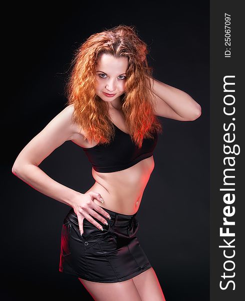 Portrait of a sexual redhead girl in a black bra and black leather skirt on a dark background