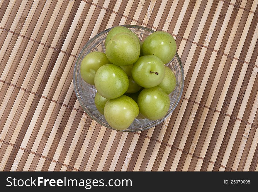 Fresh green plums in the plate and ground  on bamboo background