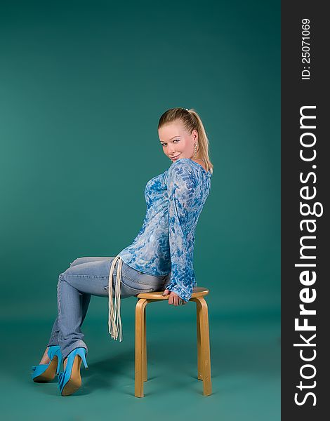 girl in a blue blouse and jeans, sitting on a chair, turquoise background in studio