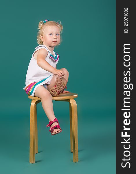 A girl in white dress sitting on a chair on the turquoise background in studio