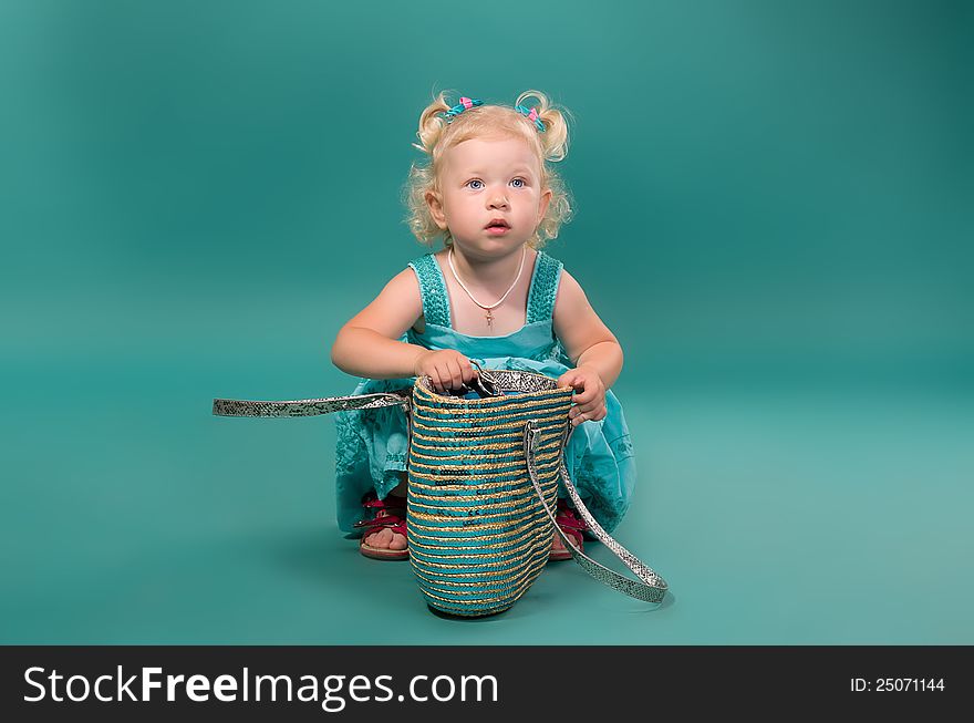 Little girl sitting near the ladies' bags on the turquoise background in studio. Little girl sitting near the ladies' bags on the turquoise background in studio