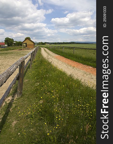 Dirt road with wooden fence in the country, rural landscape and ranch dwellings, summer landscape with a cloudy sky