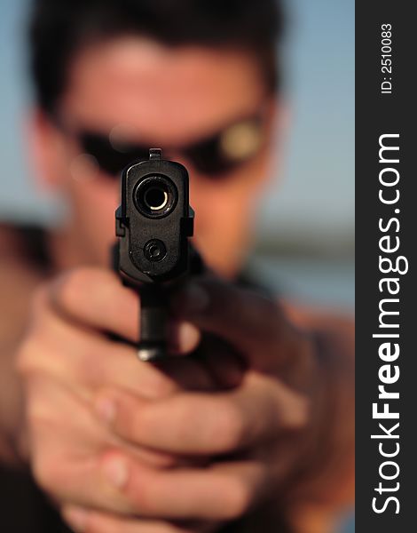 A man holding a pistol and pointing it at the camera. (This image is part of a series). A man holding a pistol and pointing it at the camera. (This image is part of a series).