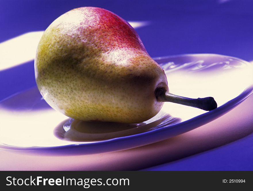 Fruit of pear lays in white plate on dark blue background. Fruit of pear lays in white plate on dark blue background