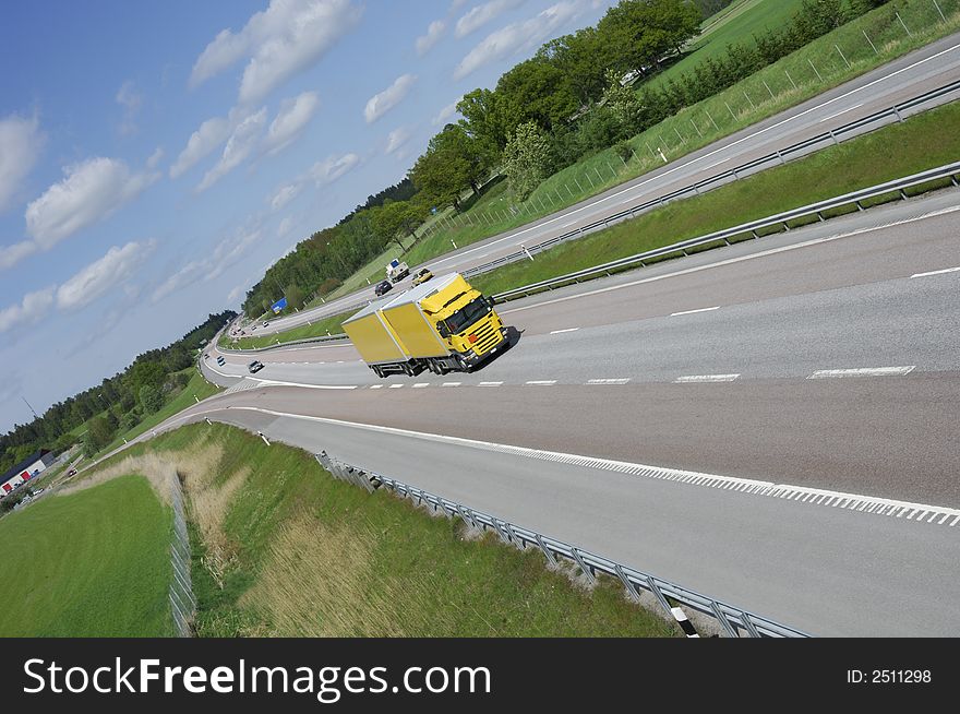 Large yellow truck speeding on highway set in a country-side surrounding, no trademarks. Large yellow truck speeding on highway set in a country-side surrounding, no trademarks