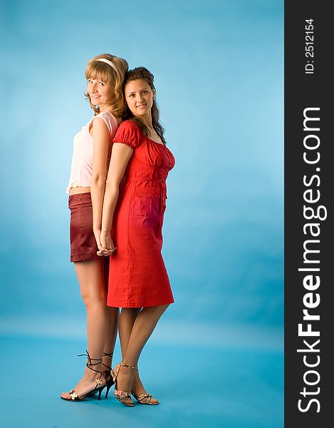 Two girls talk and pose on a blue background. Two girls talk and pose on a blue background