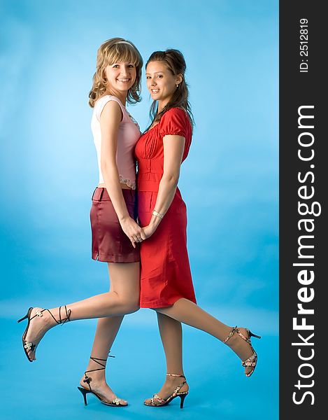 Two girls talk and pose on a blue background. Two girls talk and pose on a blue background
