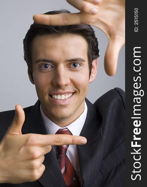 Smiling, handsome businessman. Showing his face by hands. Looking at camera. Gray background, front. Smiling, handsome businessman. Showing his face by hands. Looking at camera. Gray background, front