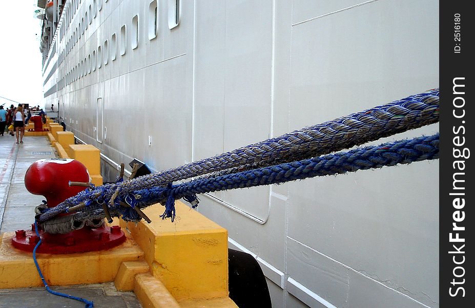 Cruise ship held at dock with blue mooring cables wrapped around red mooring bollard. Cruise ship held at dock with blue mooring cables wrapped around red mooring bollard