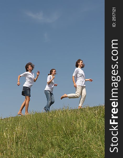 Three young nice girls running on a green grass on a background of the blue sky. Three young nice girls running on a green grass on a background of the blue sky