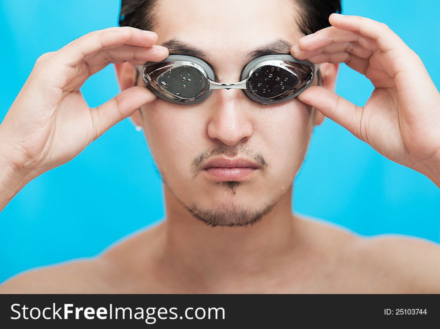 Portrait of the guy of asian appearance in swimming glasses on a blue background. Portrait of the guy of asian appearance in swimming glasses on a blue background