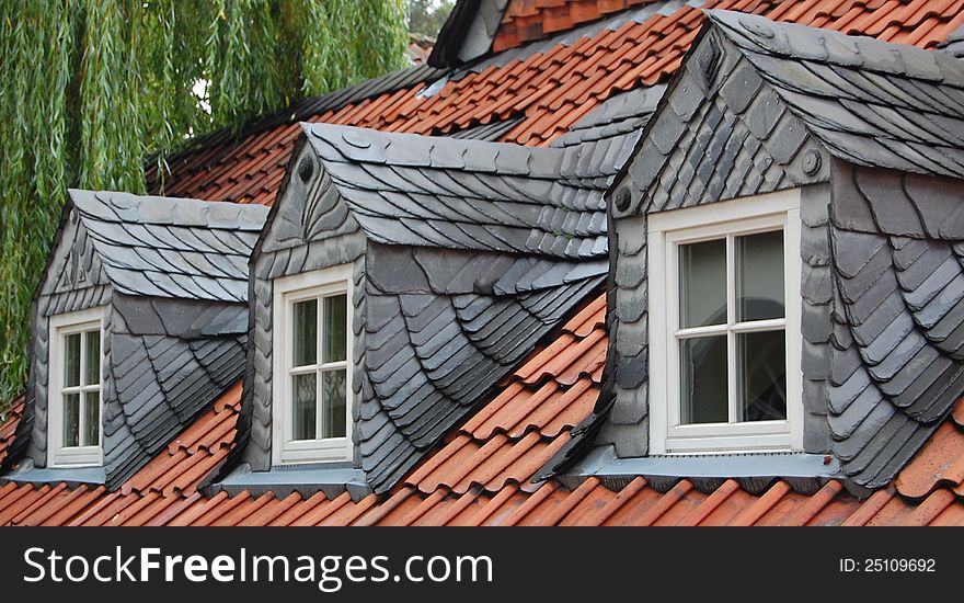 Three dormer windows with slates on red tile roof, characteristic of old houses in the Harzen capital, Goslar, Germany. Green willow in the back. Three dormer windows with slates on red tile roof, characteristic of old houses in the Harzen capital, Goslar, Germany. Green willow in the back