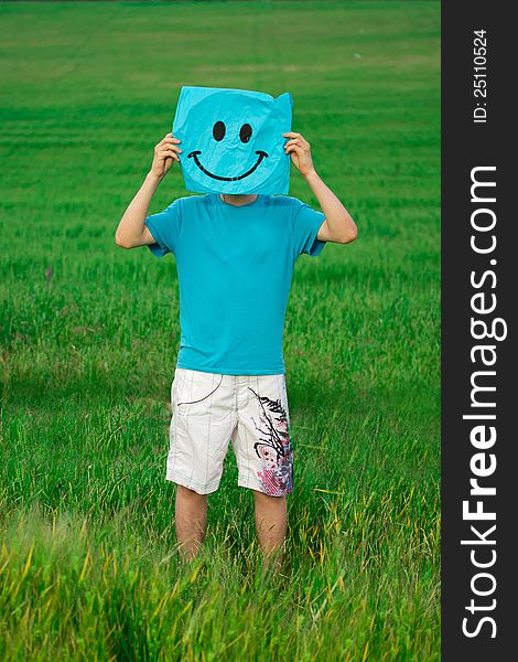 Happy young man in the summer field holds a rectangle with a painted smiley opposite face. Happy young man in the summer field holds a rectangle with a painted smiley opposite face