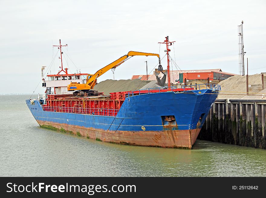 Photo of a huge cargo ship in harbour with crane off-loading aggregates onto quayside. Photo of a huge cargo ship in harbour with crane off-loading aggregates onto quayside.