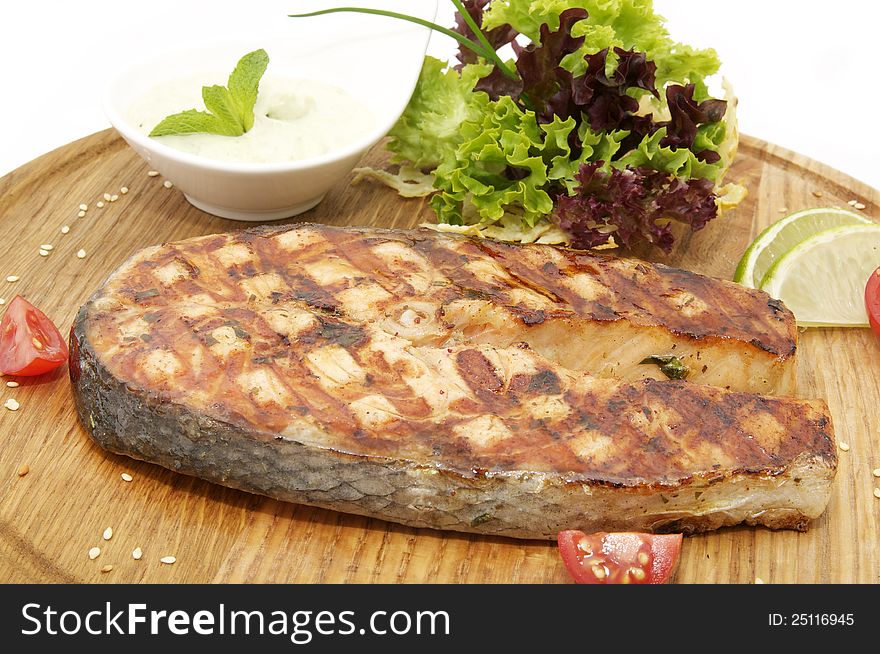 Salmon steak cooking on the grill with fresh herbs and sauce