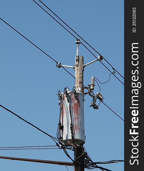 Top of an old wooden electrical pole with wires, connectors, and a transformer. Isolated against a blue sky. Top of an old wooden electrical pole with wires, connectors, and a transformer. Isolated against a blue sky.