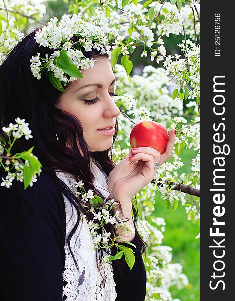 Young woman holding apple against the backdrop of flowering trees