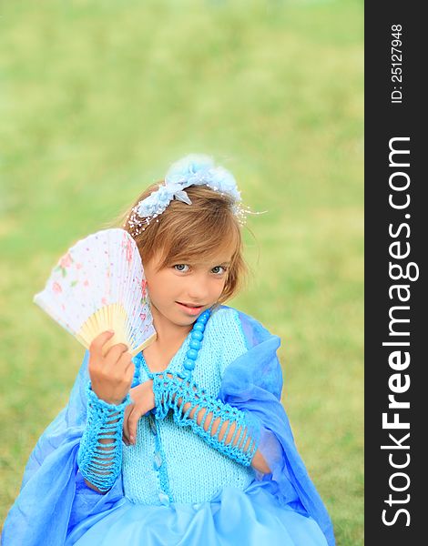 Looking like a princess. Little girl with fan in blue dress