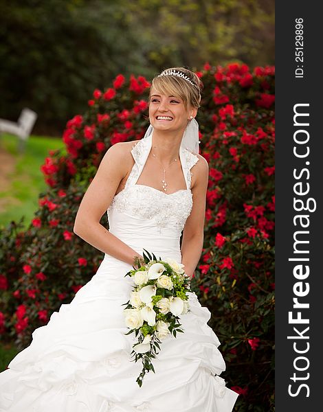 Young bride is laughing and standing in front of nice red roses and holding a nice yellow roses bouquet in her hands. she starts dancing after her wedding ceremony. Young bride is laughing and standing in front of nice red roses and holding a nice yellow roses bouquet in her hands. she starts dancing after her wedding ceremony