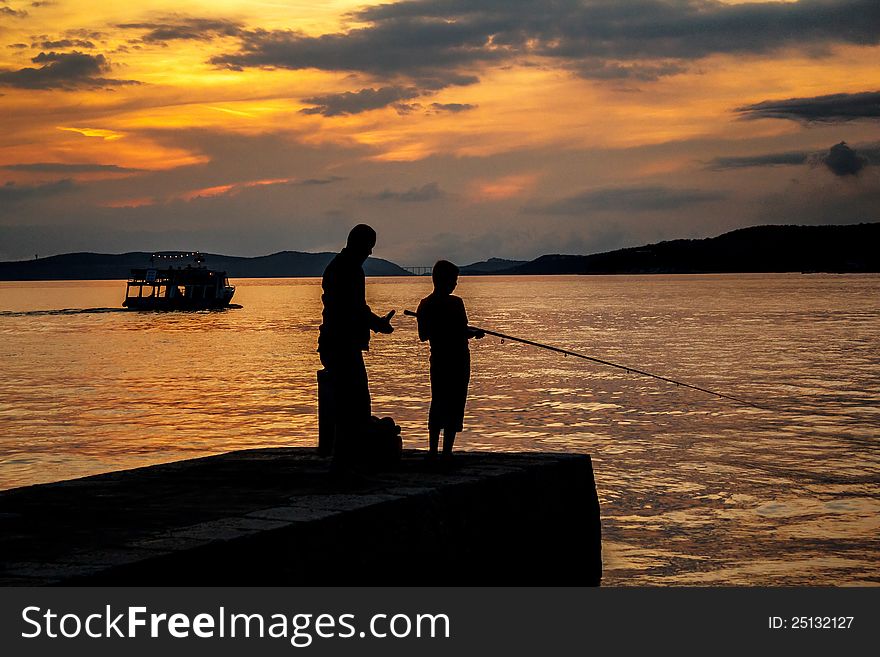 Silhouettes of father and his son fishing on sea