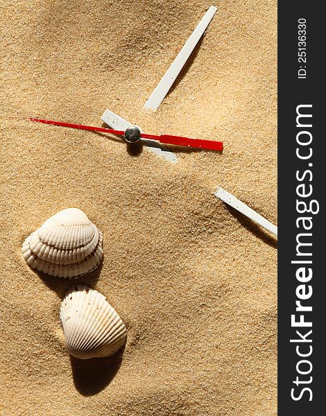 Time concept. Two seashells near clock hands on sand surface. Time concept. Two seashells near clock hands on sand surface