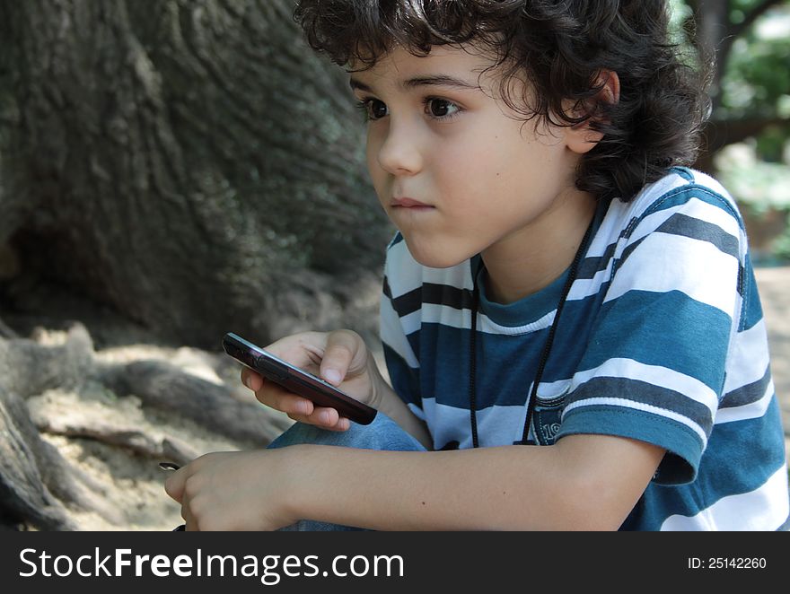 Beautiful curly child playing with cellphone sitting in the park. Beautiful curly child playing with cellphone sitting in the park