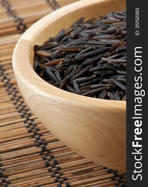 Wild brown rice in wooden bowl isolated on strawmat background