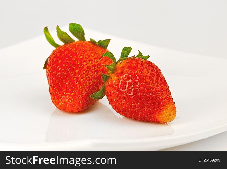 Two ripe strawberries on a white plate. Two ripe strawberries on a white plate