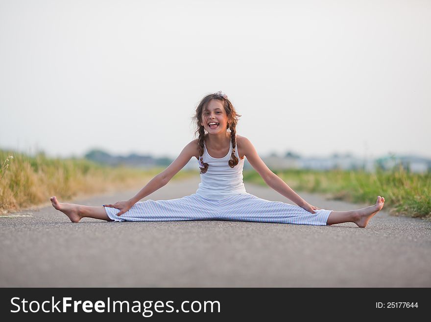 Cute young girl makes a split on a path