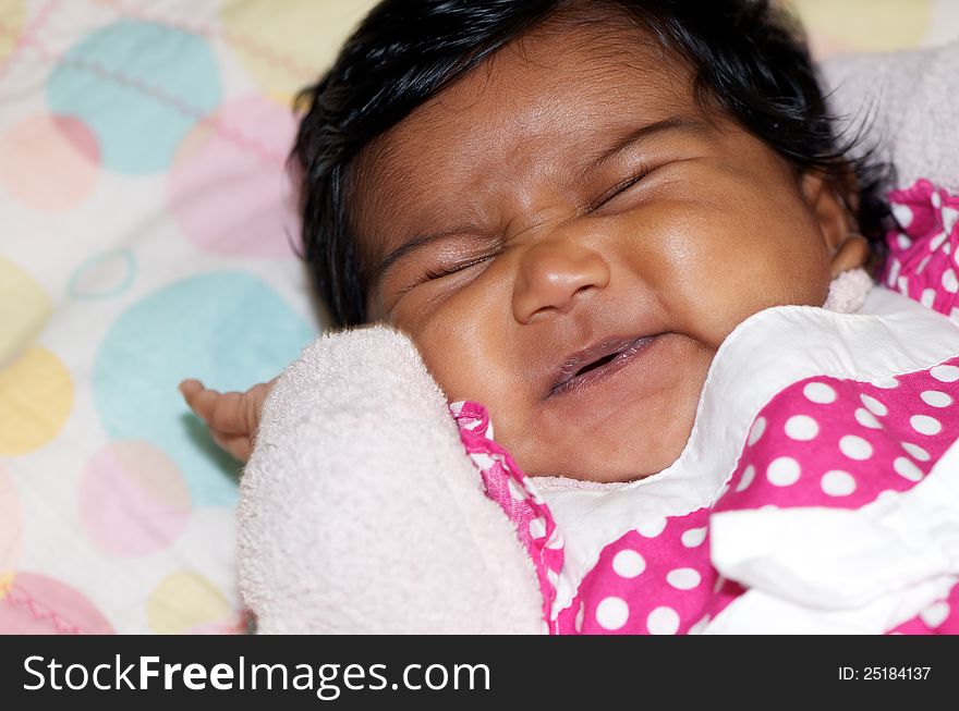 Headshot portrait of adorable newborn baby waking up and stretching, her gorgeous little face all scrunched up