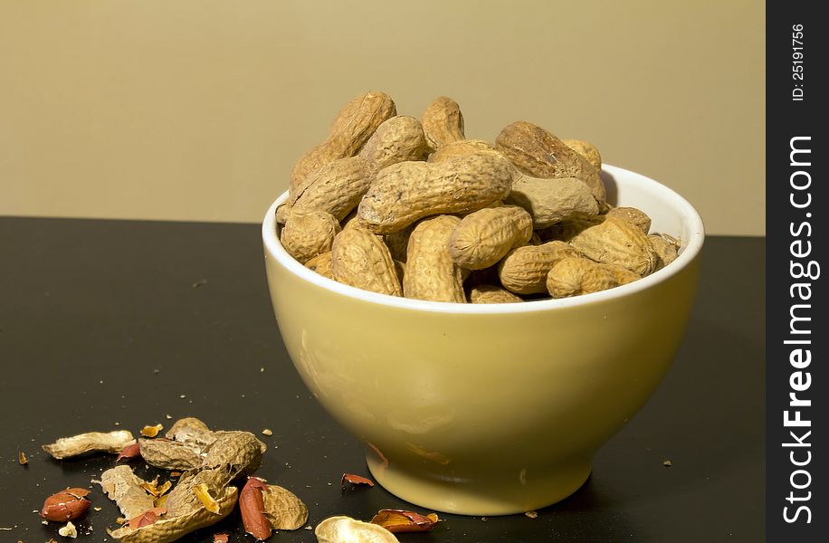 A bowl of peanuts in shell with some leftovers shells from eaten ones