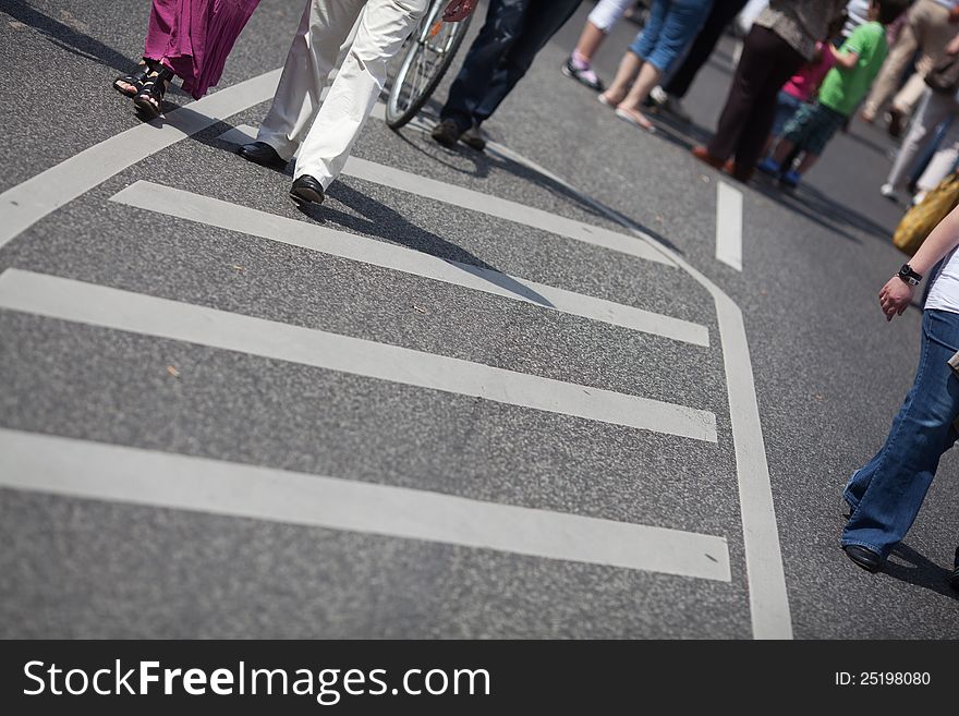 The picture shows the legs of a crowd of people that walks on the street during a street festival. The picture shows the legs of a crowd of people that walks on the street during a street festival
