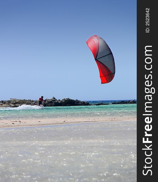 A kitesurfer with a red kite surfing the shoreline of Creete Greece. A kitesurfer with a red kite surfing the shoreline of Creete Greece