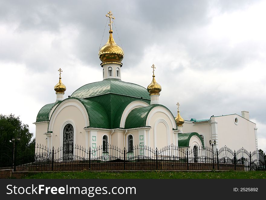 White Christian church with the gilt domes and a green roof.