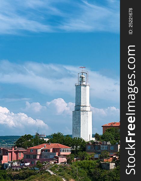 Vertical photo of a white lighthouse. It is located in the city and there are buildings around it. The sky is vivid and there are clouds. Vertical photo of a white lighthouse. It is located in the city and there are buildings around it. The sky is vivid and there are clouds.