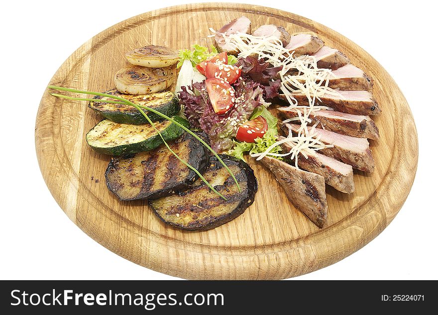 Meat roasted on a grill with vegetables on a wooden plate