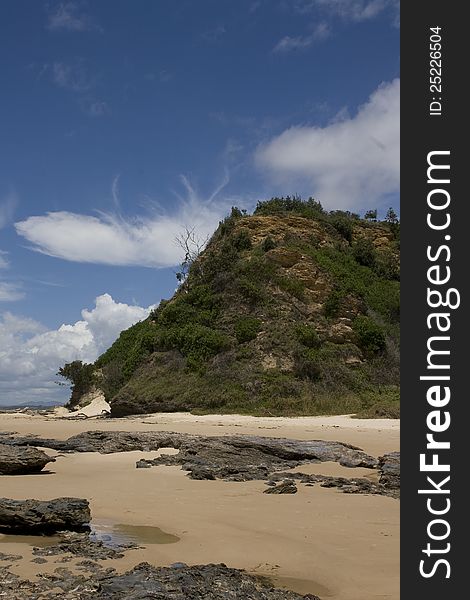 Image shows sand rocks and sky framing a rugged sea cliff in northern NSW Australia. Image shows sand rocks and sky framing a rugged sea cliff in northern NSW Australia