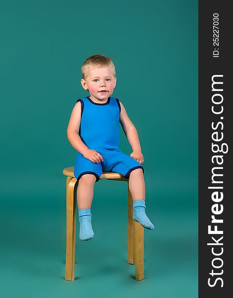 A boy in a blue clothes sitting on a wooden chair, on a green background