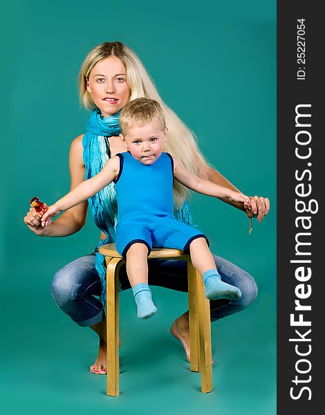 Portrait of blonde mom in jeans and a scarf and a son in a blue suit, a green background. Portrait of blonde mom in jeans and a scarf and a son in a blue suit, a green background