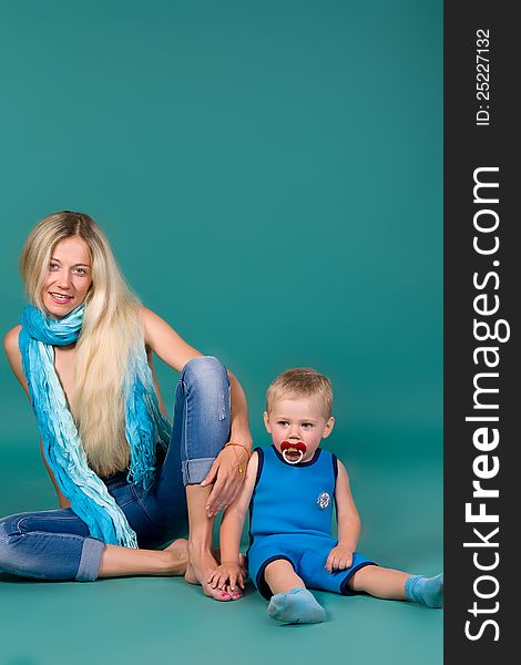 Portrait of blonde mom in jeans and a scarf and a son in a blue suit, a green background. Portrait of blonde mom in jeans and a scarf and a son in a blue suit, a green background