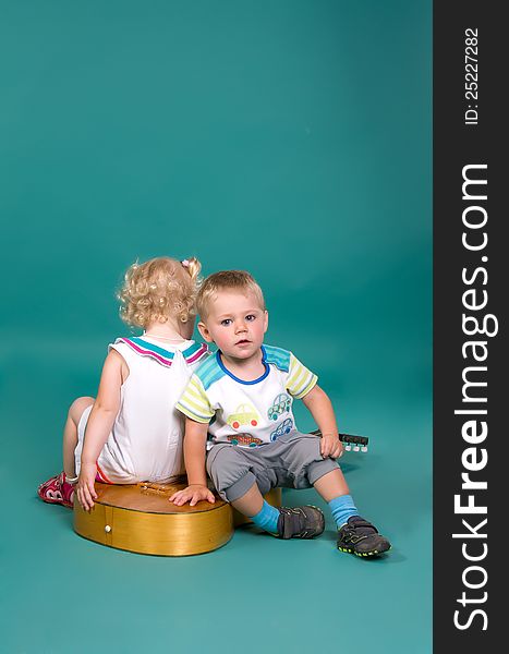 Girl and boy sitting on the guitar back to back, on a green background