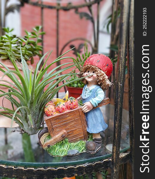 A gardening decorative figure, a little girl pushes a wheelbarrow next to a plant