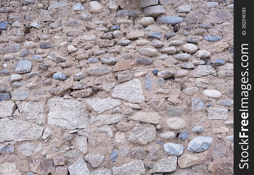 Background image of wall texture made of rocks and pebbles made of mud.