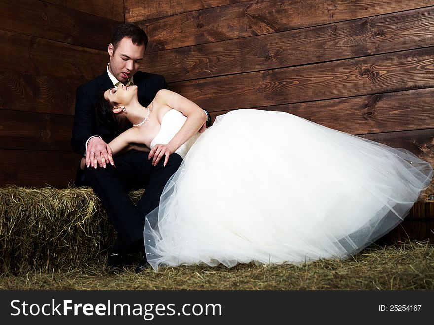 Bride lying on groom's lap in barn with hay. Bride lying on groom's lap in barn with hay