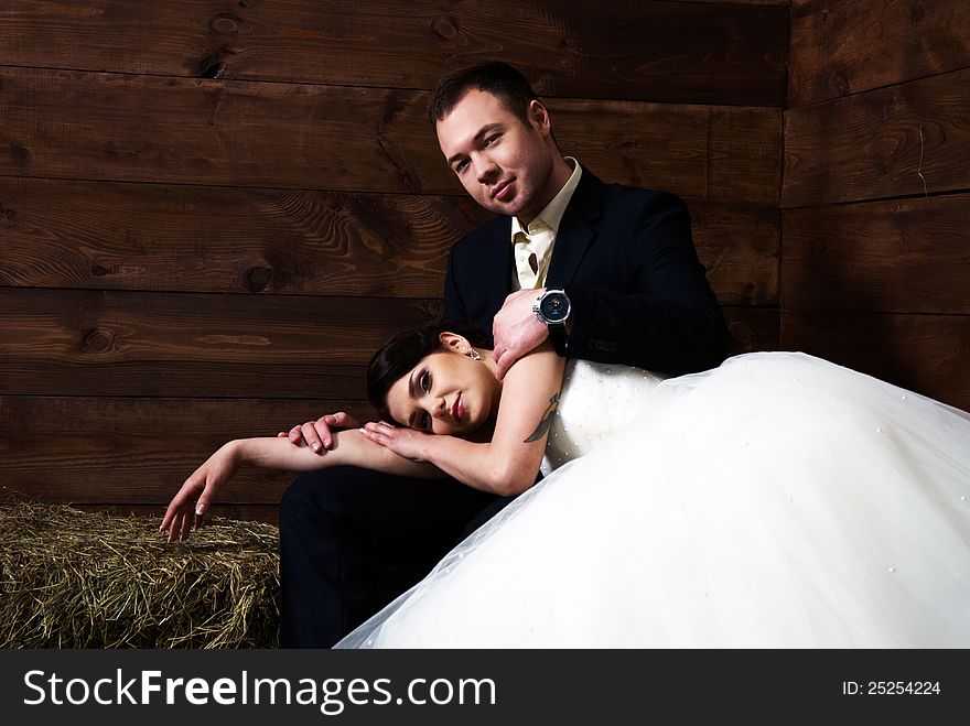 Bride lying on groom's lap in barn with hay. Bride lying on groom's lap in barn with hay