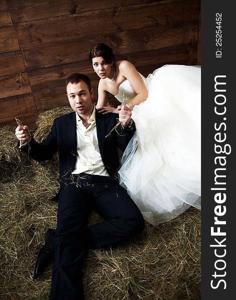 Couple in their wedding clothes in barn with hay fooling with each other