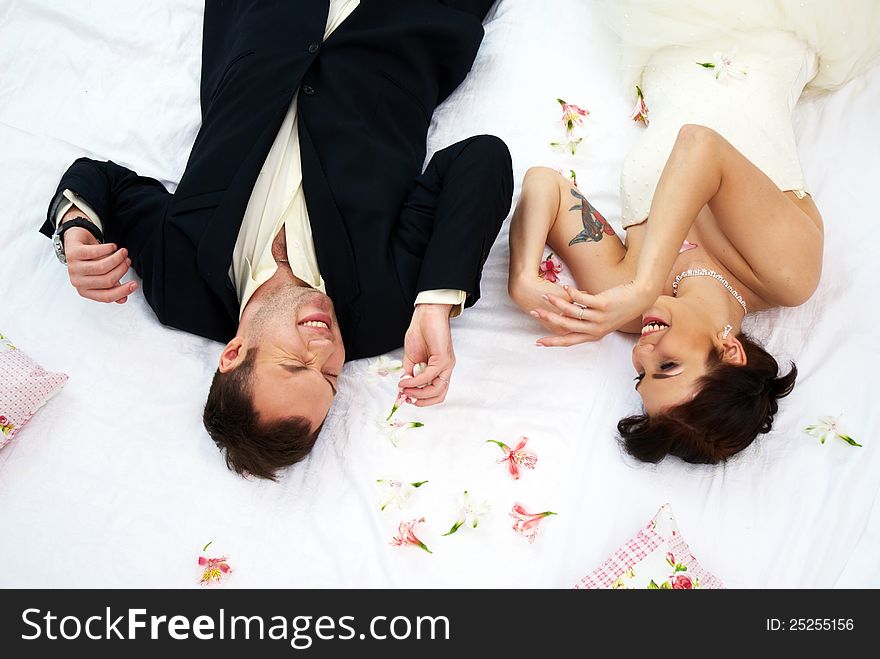 Bride And Groom Lying In Bedroom With Orchids