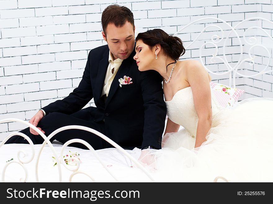 Bride and groom sitting on bed in stylish bedroom. Bride and groom sitting on bed in stylish bedroom