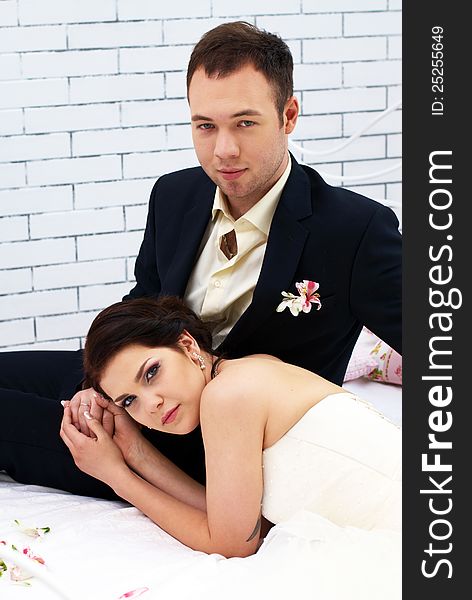 Bride and groom sitting on bed in bedroom