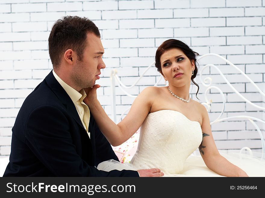 Bride and groom sitting on bed in bedroom